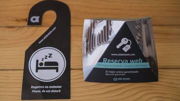A black hang tag with a 'PZ' symbol and text 'Rogamos no molestar Please, do not disturb' and a black box with a hotel logo and text 'Reserva web' and 'El mejor precio garantizado Best price guaranteed'.