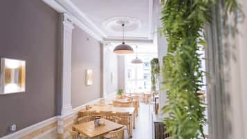 Un couloir avec des tables et des chaises en bois, des colonnes blanches et des lampes suspendues.