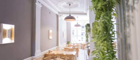A corridor with wooden tables and chairs, white columns, and hanging pendant lights.