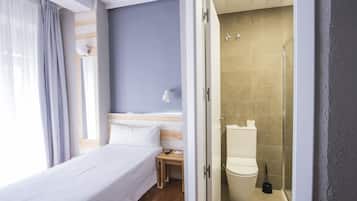 Et hotelværelse med seng, natbord og bruseområde.