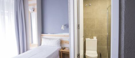 Habitación de hotel con cama, mesita de noche y zona de ducha.