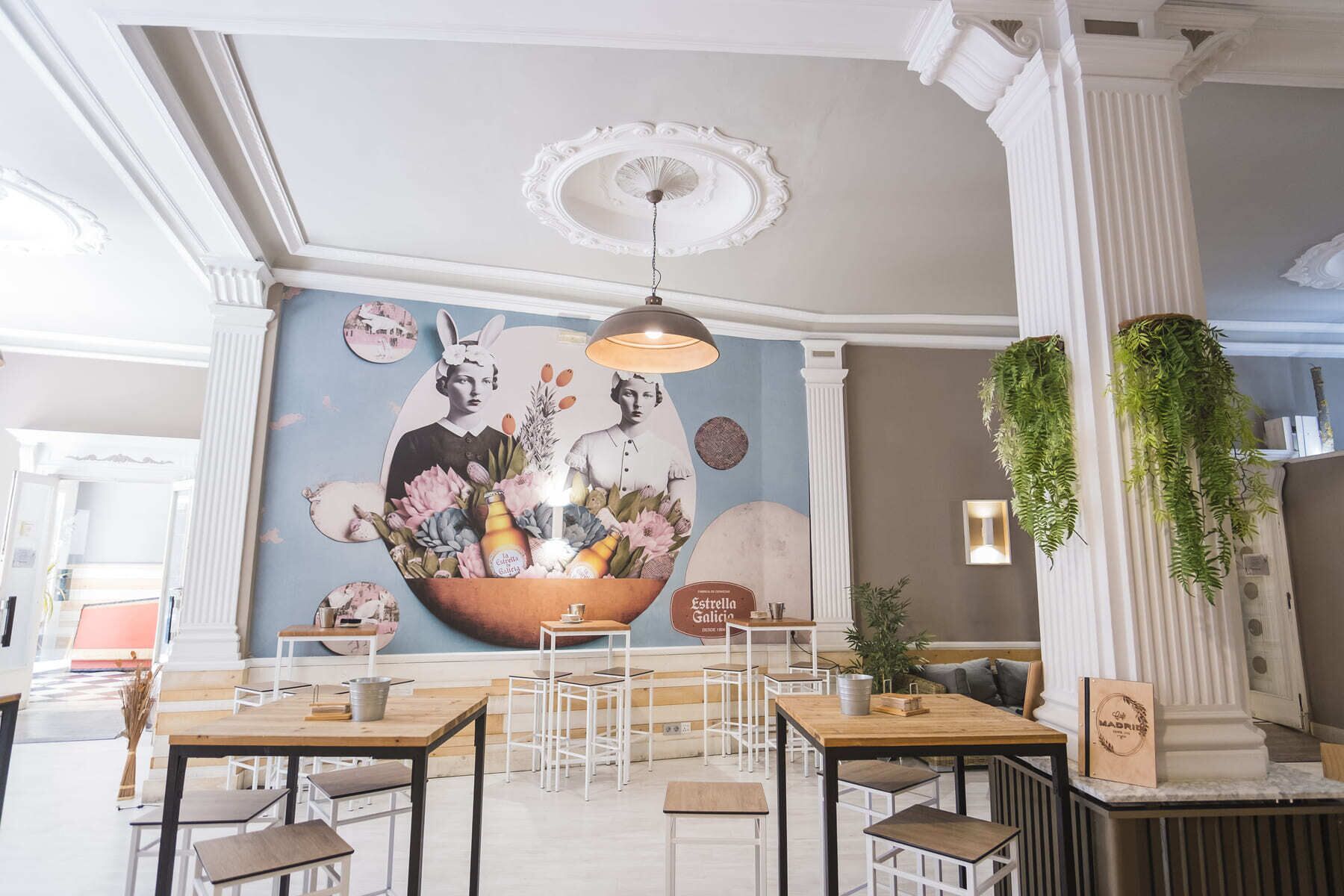 A restaurant interior with a mural, hanging plants, and a variety of seating arrangements.