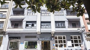 Un hotel de varios pisos con fachada moderna, amplias ventanas y un área de estar en la planta baja con sillas.