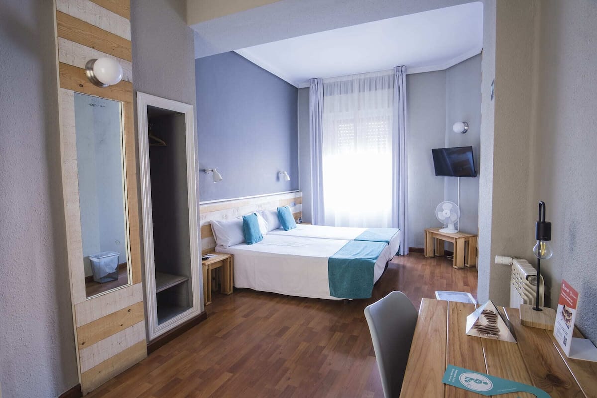 Ein Hotelzimmer mit einem Bett, einem Schreibtisch, einem Stuhl, einem Fernseher, einer Lampe und einem Fenster mit Vorhängen.