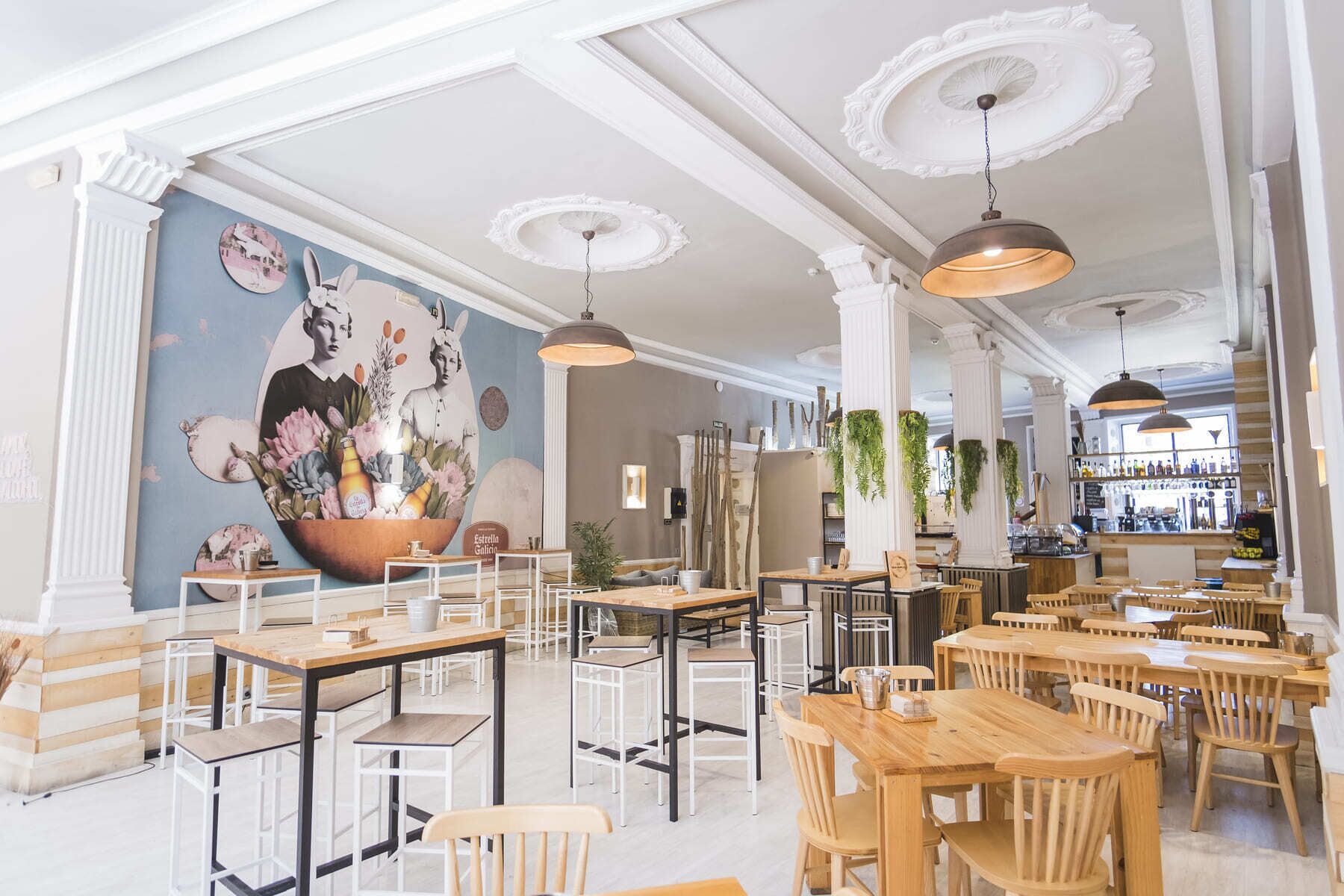 A restaurant interior with wooden tables and chairs, a mural on the wall, and hanging plants.