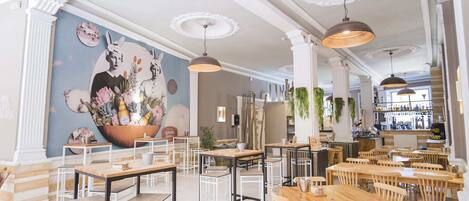 A restaurant interior with wooden tables and chairs, a mural on the wall, and hanging plants.