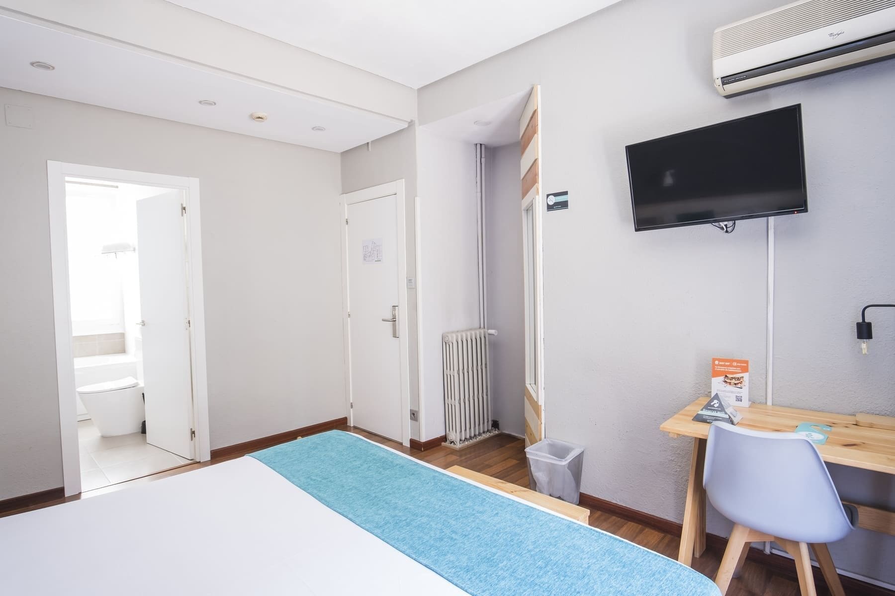 Ein Hotelzimmer mit Bett, Schreibtisch mit Stuhl, Fernseher, Klimaanlage und Heizkörper.