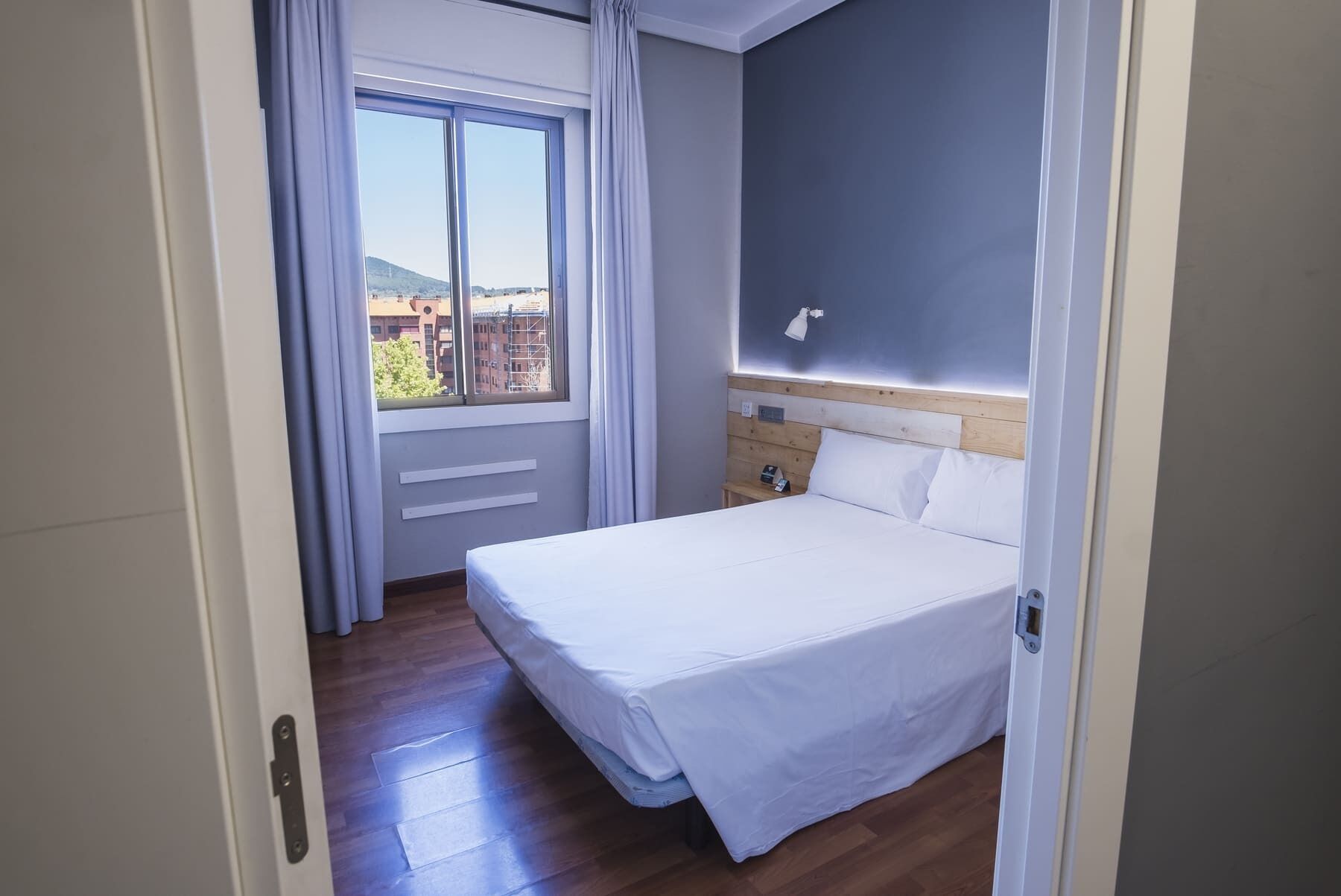 A hotel room with a bed, a nightstand, a lamp, and a window with curtains.
