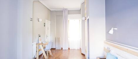 Habitación de hotel con cama, escritorio con silla, radiador y ventana con cortinas.