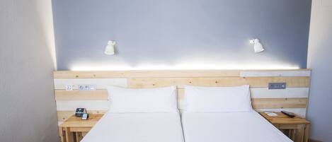 A double bed with white linens, wooden headboard, bedside tables with lamps, and a power outlet on the wall.