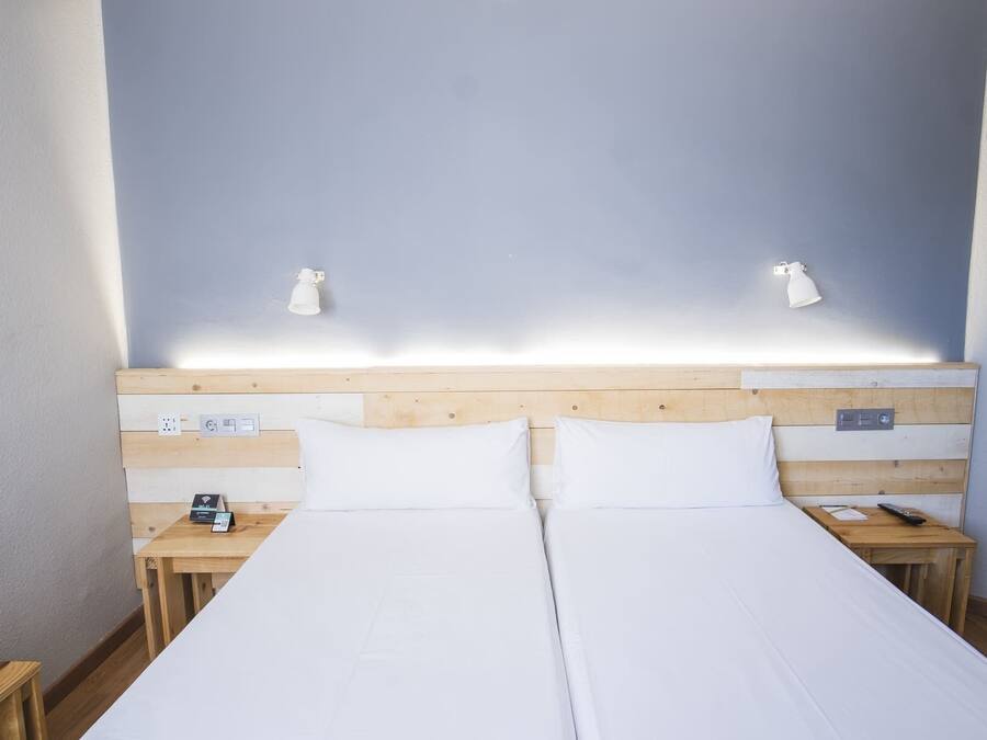 A double bed with white linens, wooden headboard, bedside tables with lamps, and a power outlet on the wall.