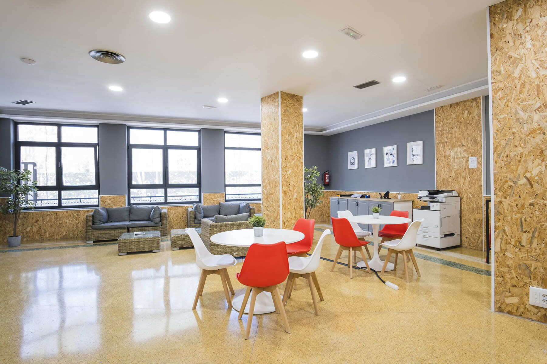Una oficina amplia con diseño moderno, que incluye una mesa redonda central con sillas, una kitchenette y grandes ventanales que brindan luz natural.