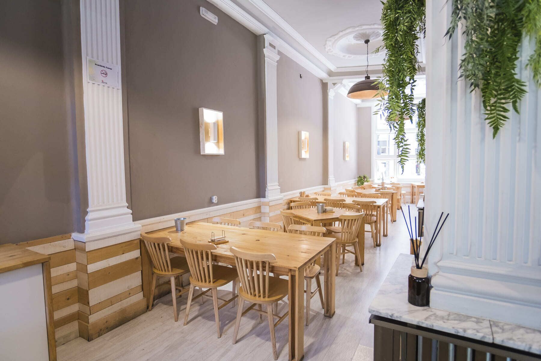 Un restaurant avec des tables et des chaises en bois, un comptoir en marbre et des plantes suspendues.