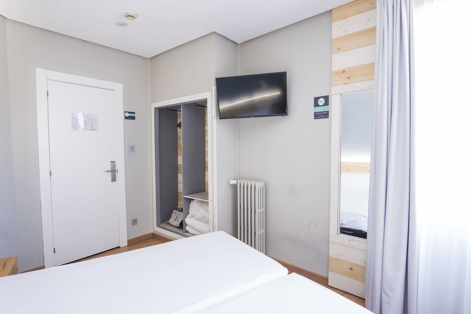 A hotel room with a bed, a television mounted on the wall, a wardrobe, and a radiator.