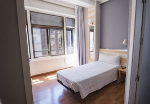 A bedroom with a bed, a bedside table, a lamp, and a window with curtains.