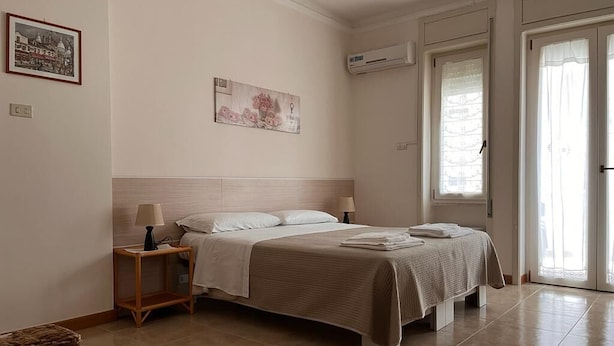 A bedroom with a bed, bedside tables, a lamp, a wall-mounted air conditioner, and a door with a glass panel. - B&B Kalypso (Gallipoli)