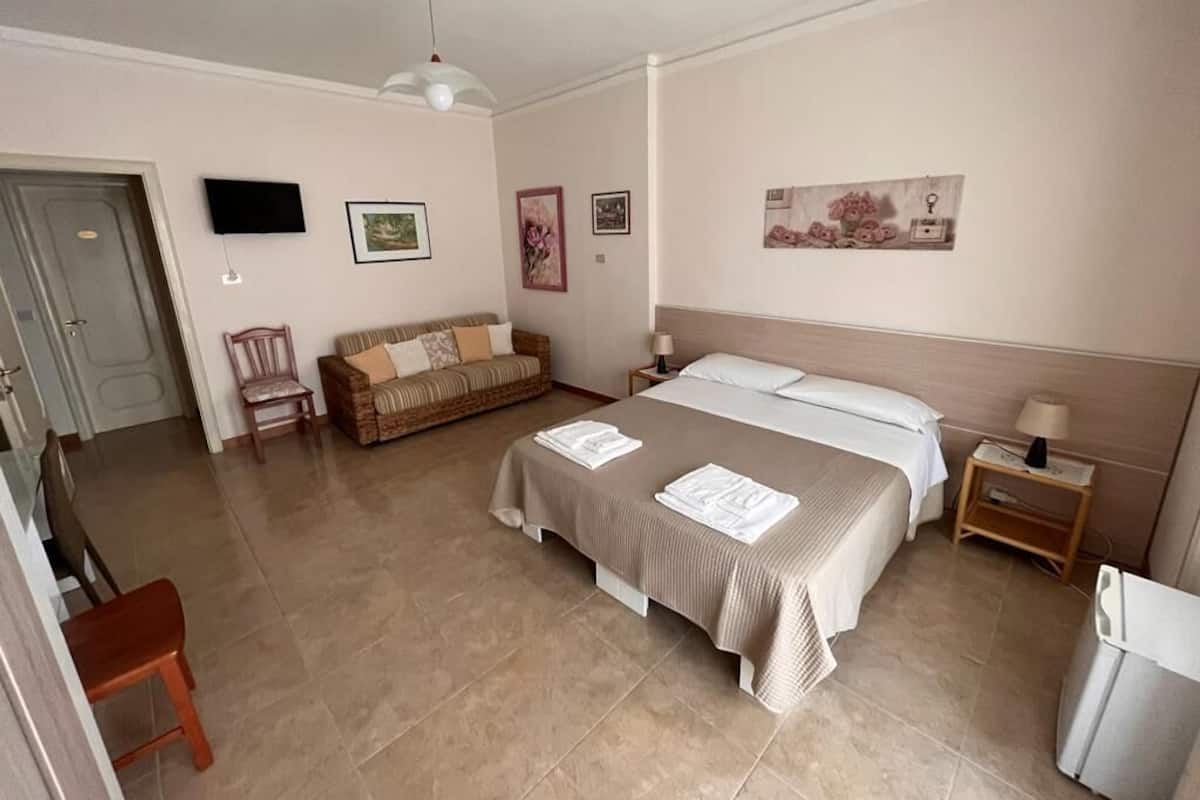 A bedroom with a bed, a sofa, a TV, and a door.