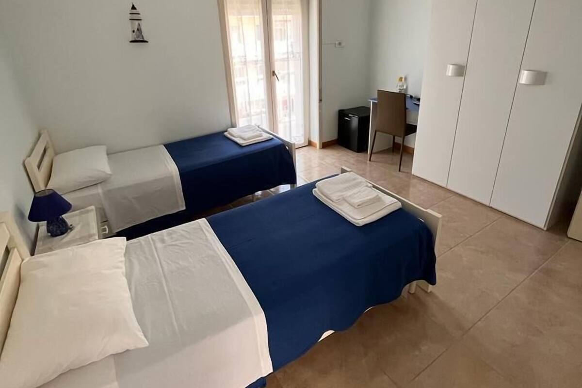 A bedroom with two beds, a desk, a chair, and a wardrobe.