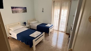 A room with two beds, a ceiling fan, a window with curtains, and a door. - B&B Kalypso (Gallipoli)