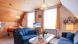 Een gezellige woonkamer met houten plafond, een televisie, een eethoek met tafel en stoelen, en een bank.