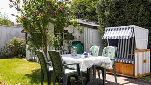 Een terras met een tafel en stoelen, een gestreept zonnescherm en een kleine schuur.