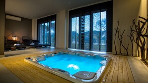 Piscina interior moderna com deck de madeira, grandes janelas e vista para árvores.