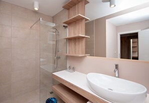 A modern bathroom with a glass shower enclosure, a white sink, and wooden shelves.