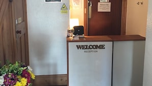 Un comptoir d’accueil avec une pancarte « Bienvenue », un avis concernant la vidéosurveillance et une indication que l’hôtel est une propriété privée.