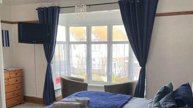 Une chambre à coucher avec un lit, une télévision, une fenêtre avec des rideaux, une commode et une chaise.