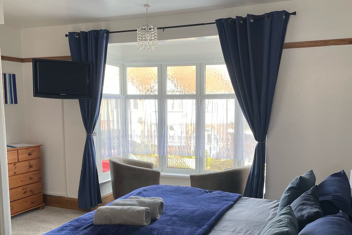 A bedroom with a bed, a TV, a window with curtains, a dresser, and a chair.