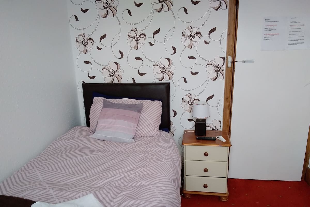 A neatly made bed with patterned bedding, a bedside table with a lamp, and a wall with floral wallpaper.