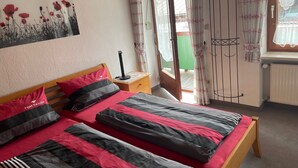 Ein Schlafzimmer mit zwei Betten, einem Nachttisch, einem Fenster mit Vorhängen und einem Bild an der Wand.