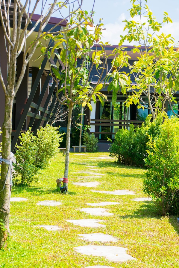 A pathway with stepping stones leading to a building with a modern design and a garden area with various plants.