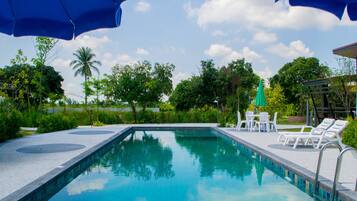 Una piscina con sillones de descanso y sombrillas, rodeada de follaje y árboles.