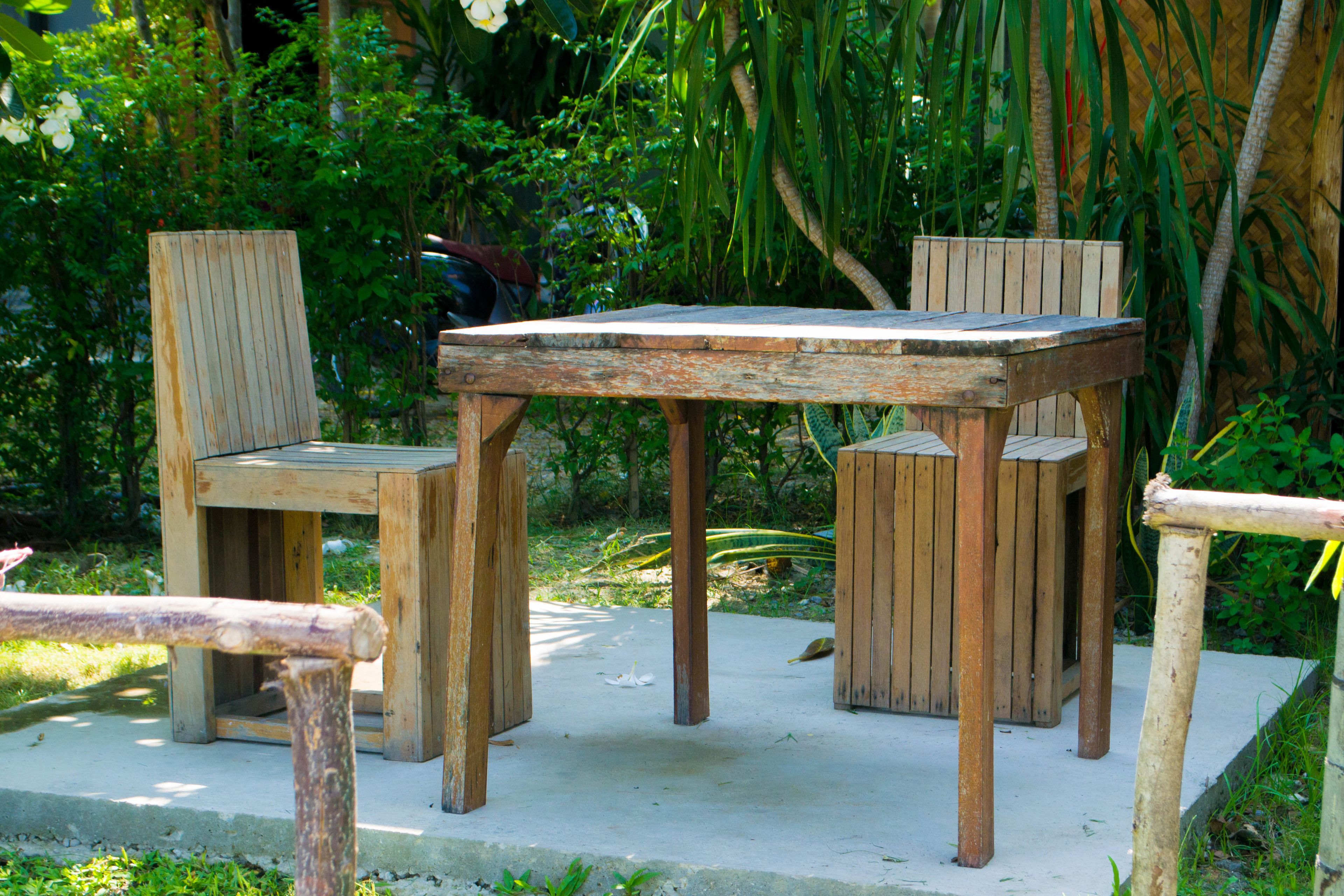 A wooden outdoor seating area with a table and chairs, surrounded by lush greenery.