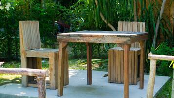 A wooden outdoor seating area with a table and chairs, surrounded by lush greenery.