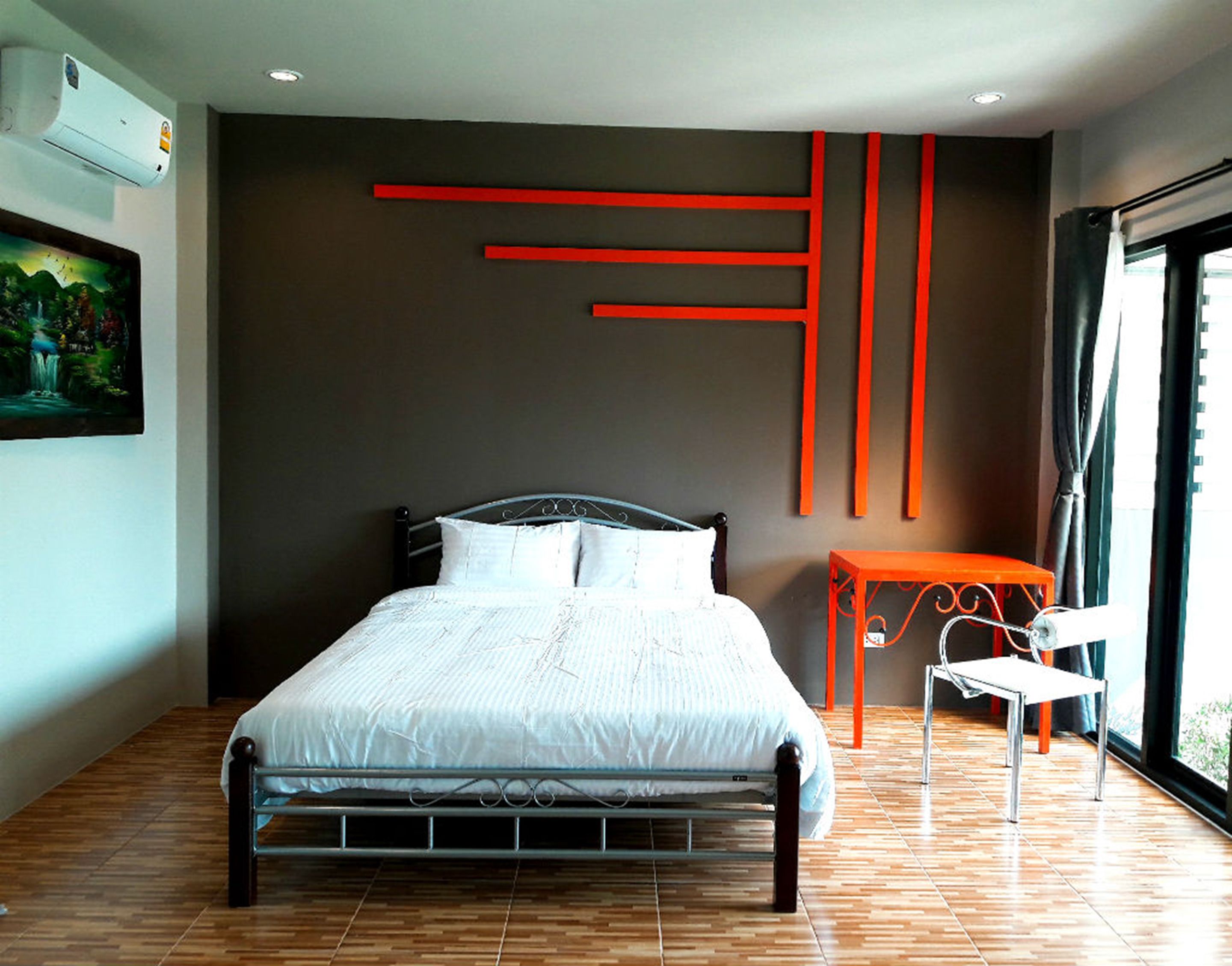 A modern bedroom with a metal bed frame, a white bedspread, and a painting of a landscape on the wall.