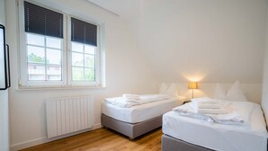 A bedroom with two beds, a window with blinds, a radiator, and a lamp. - Apartment 10 (ID 291), Germany (Sankt Peter-Ording)