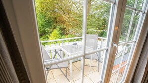 A balcony with a table and chairs, a white fence, and a view of trees and greenery. - Apartment 10 (ID 291), Germany (Sankt Peter-Ording)