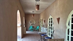 Un pasillo con suelo de ladrillo, una zona de estar con una mesa y sillas, y una puerta con diseño decorativo.