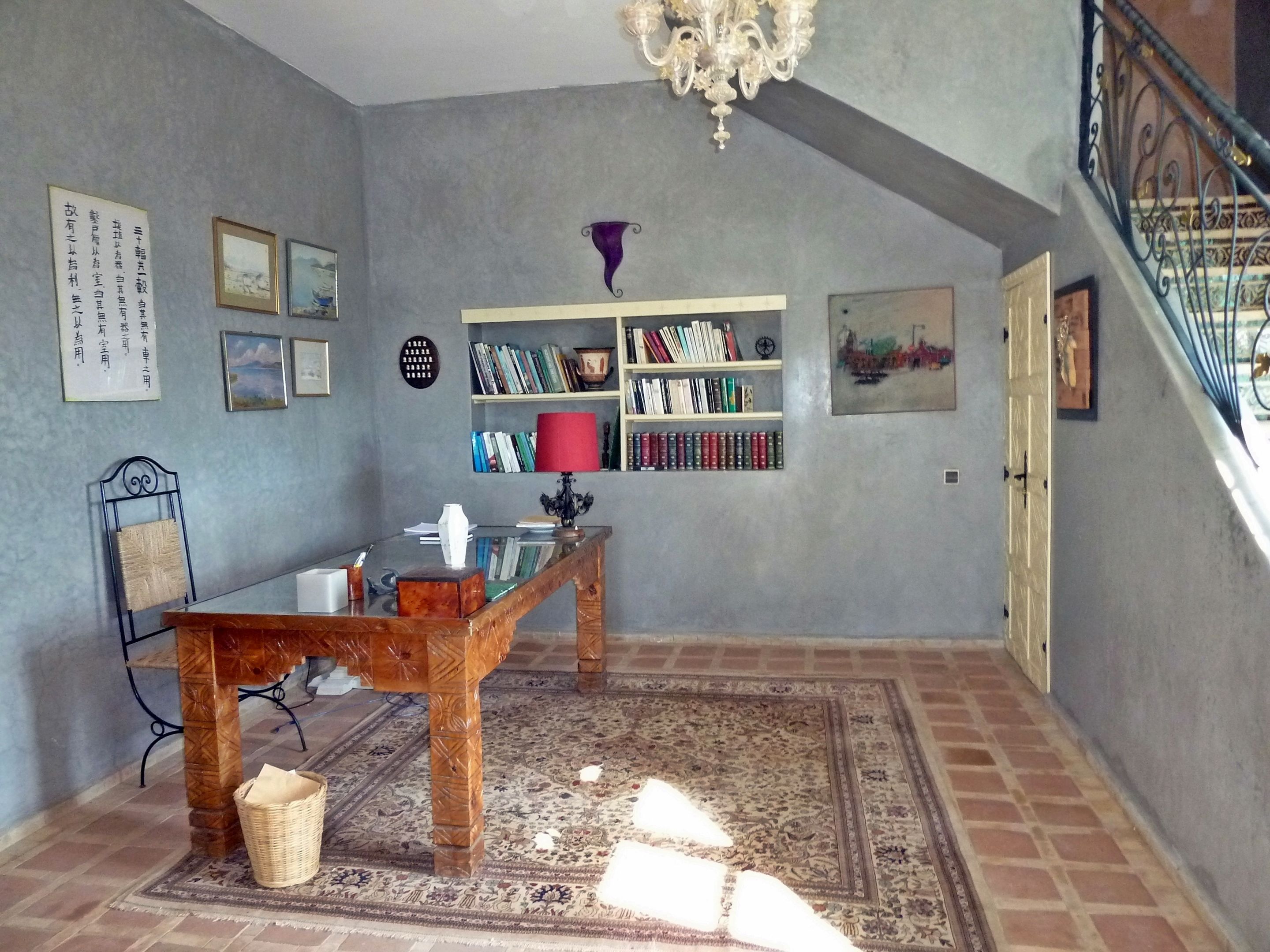 A room with a wooden desk, bookshelves, a chandelier, and a staircase.