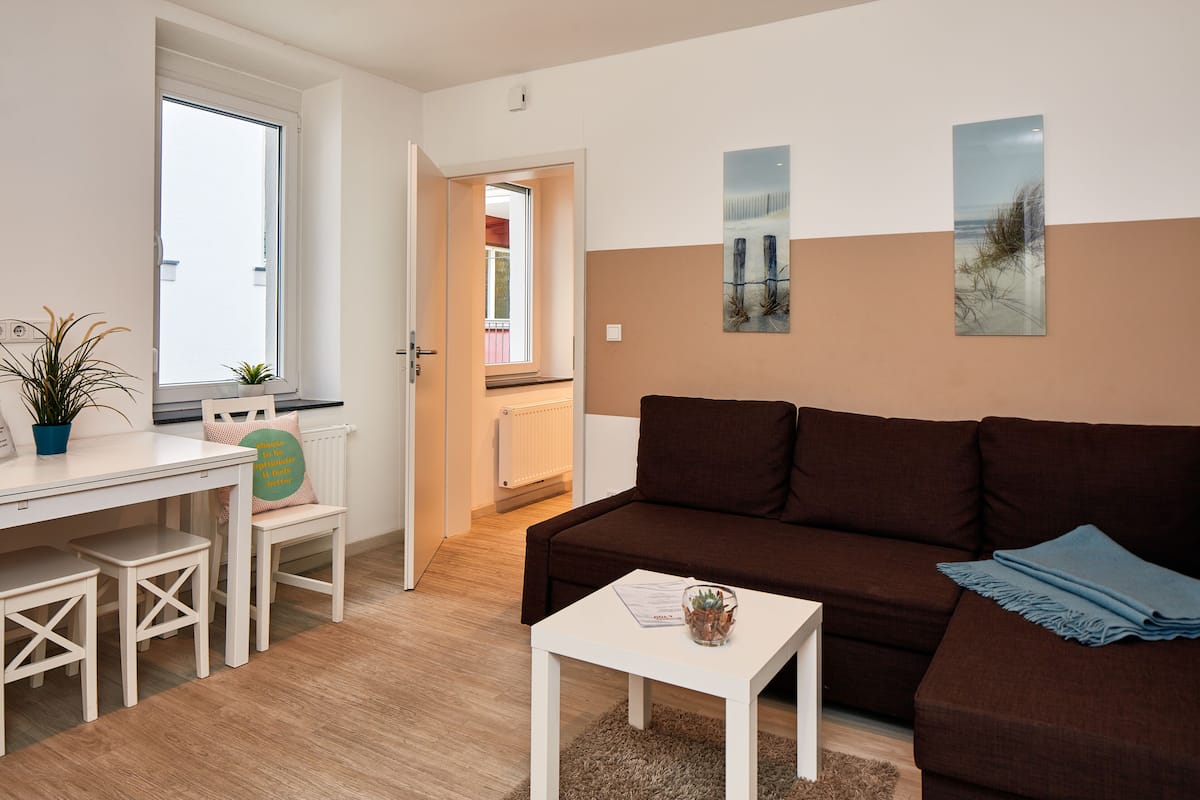 A modern living room with a brown sofa, white coffee table, and a dining area with a white table and chairs.