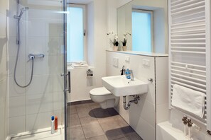 Un baño moderno con ducha de vidrio, un lavamanos blanco y un inodoro.