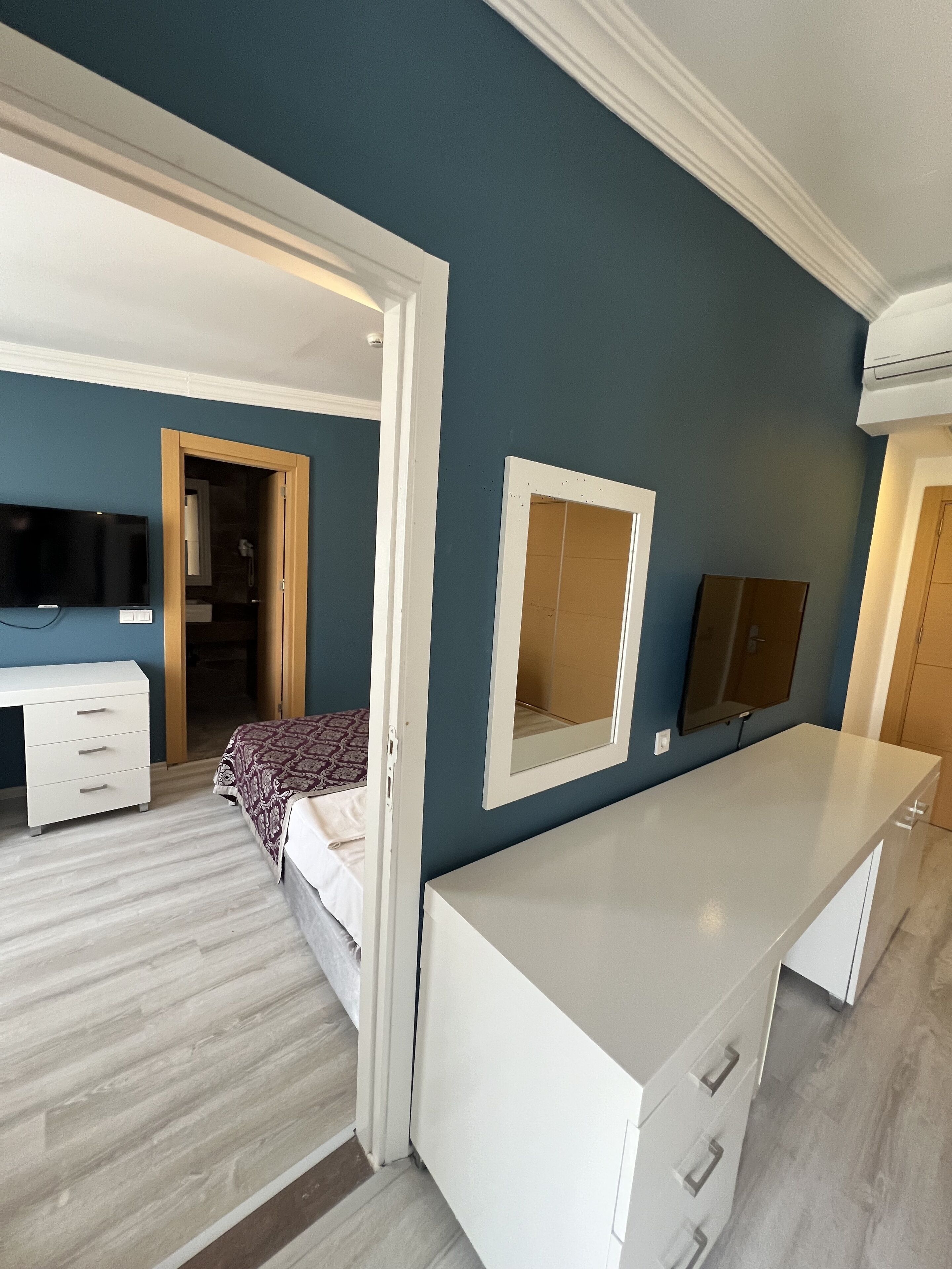 A bedroom with a bed, a dresser, a TV, and a mirror.