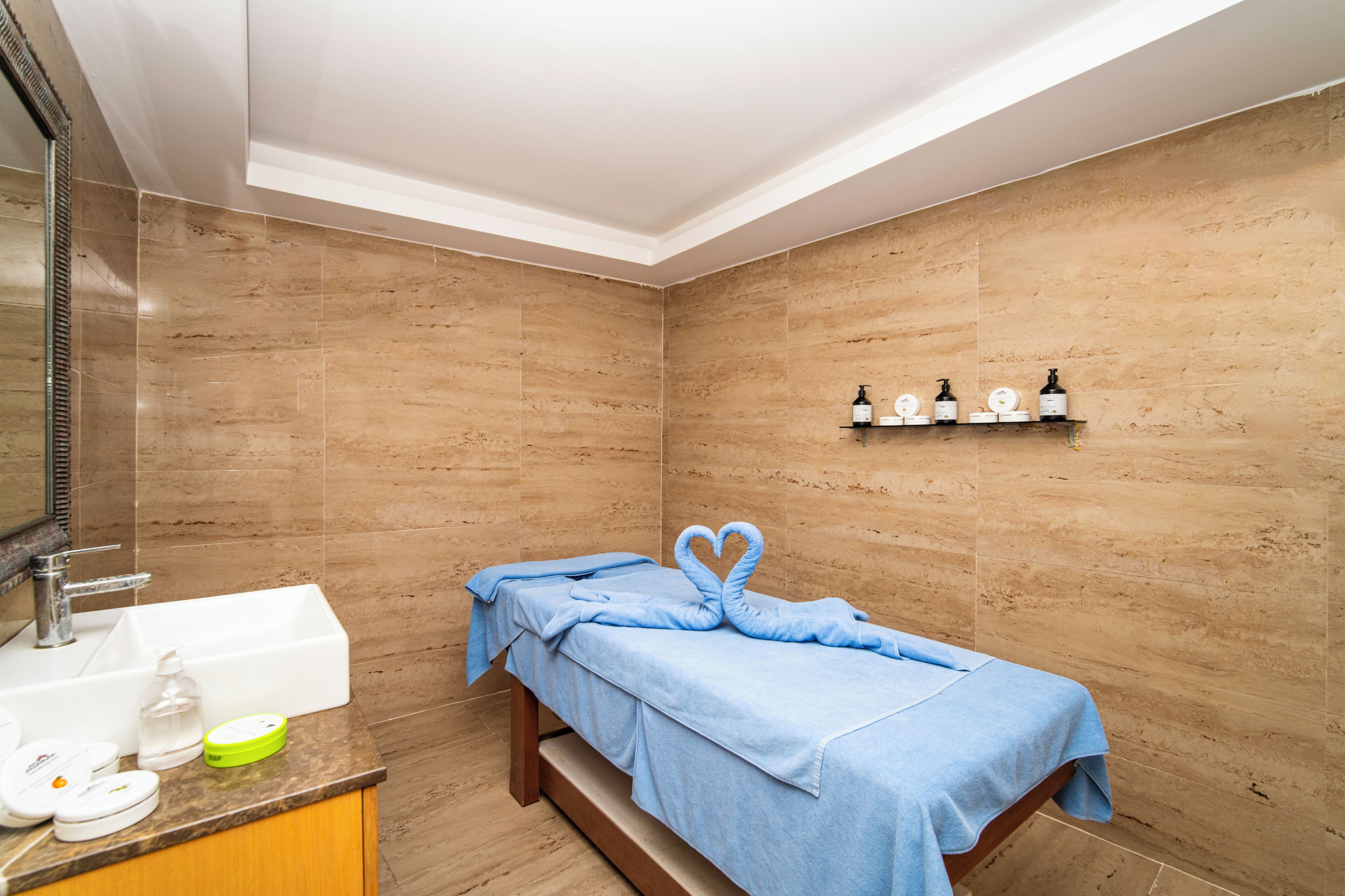A small, modern bathroom with a sink, mirror, and a bed with a towel.