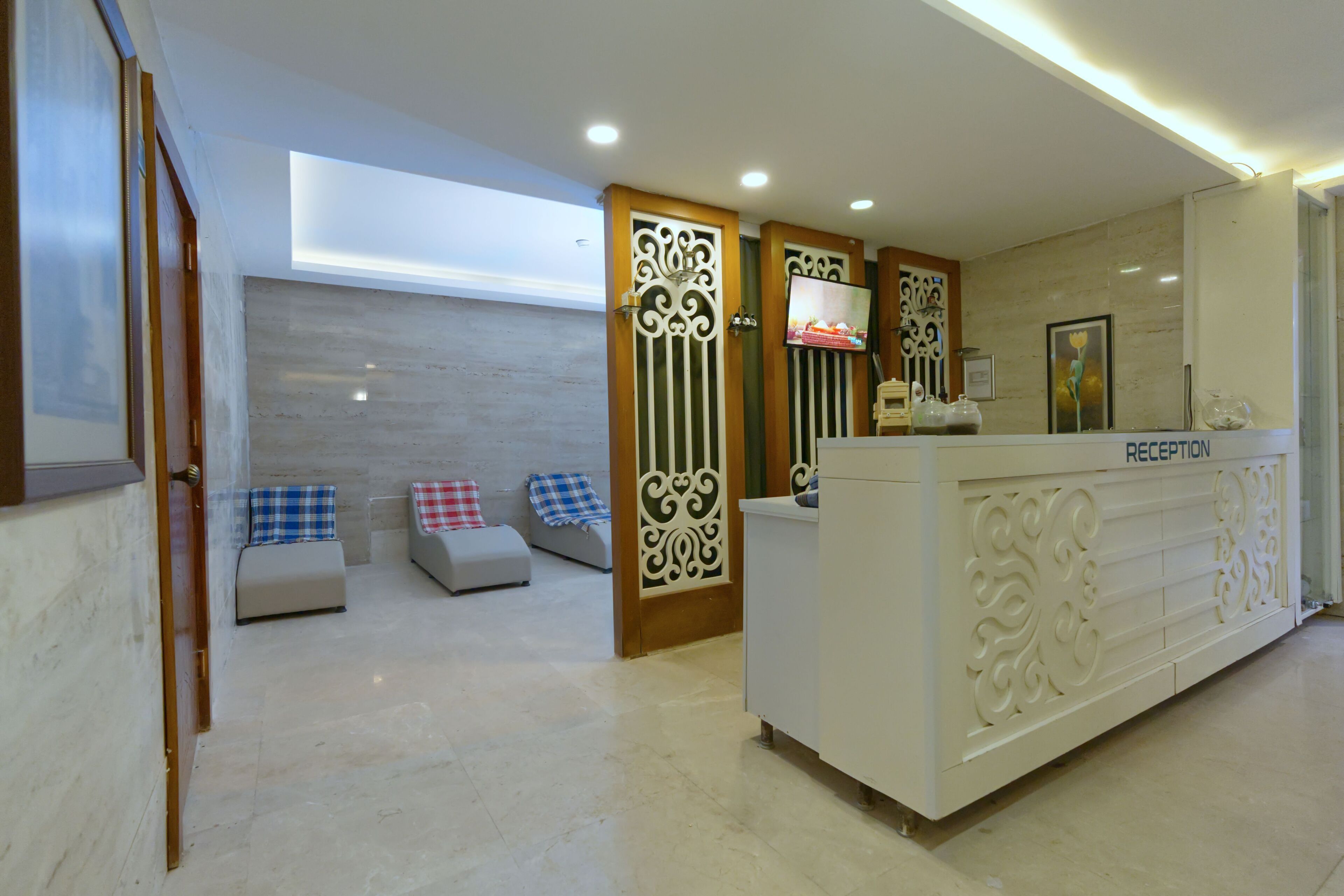 Un área de recepción con mostrador, zona de estar con cojines y televisor montado en la pared.