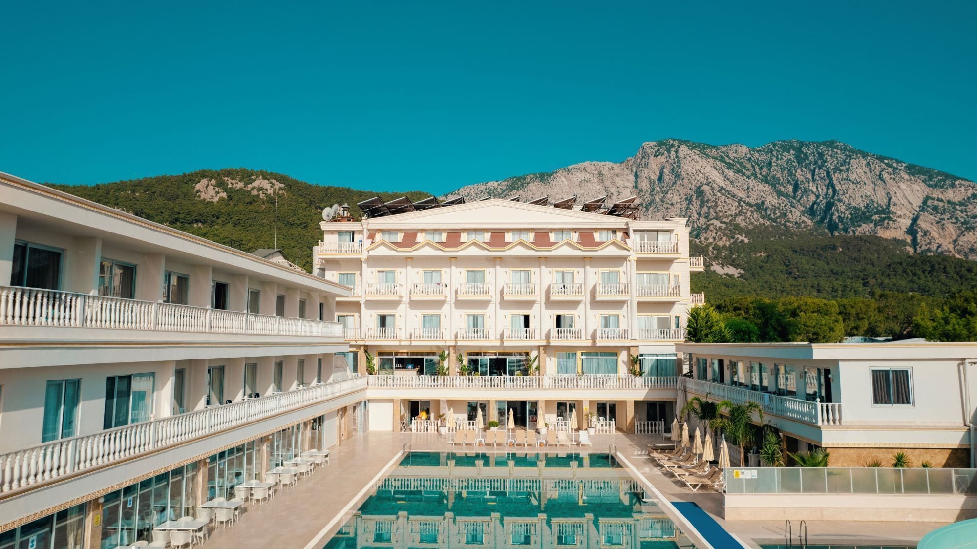 A hotel with a pool, multiple balconies, and a mountainous backdrop.