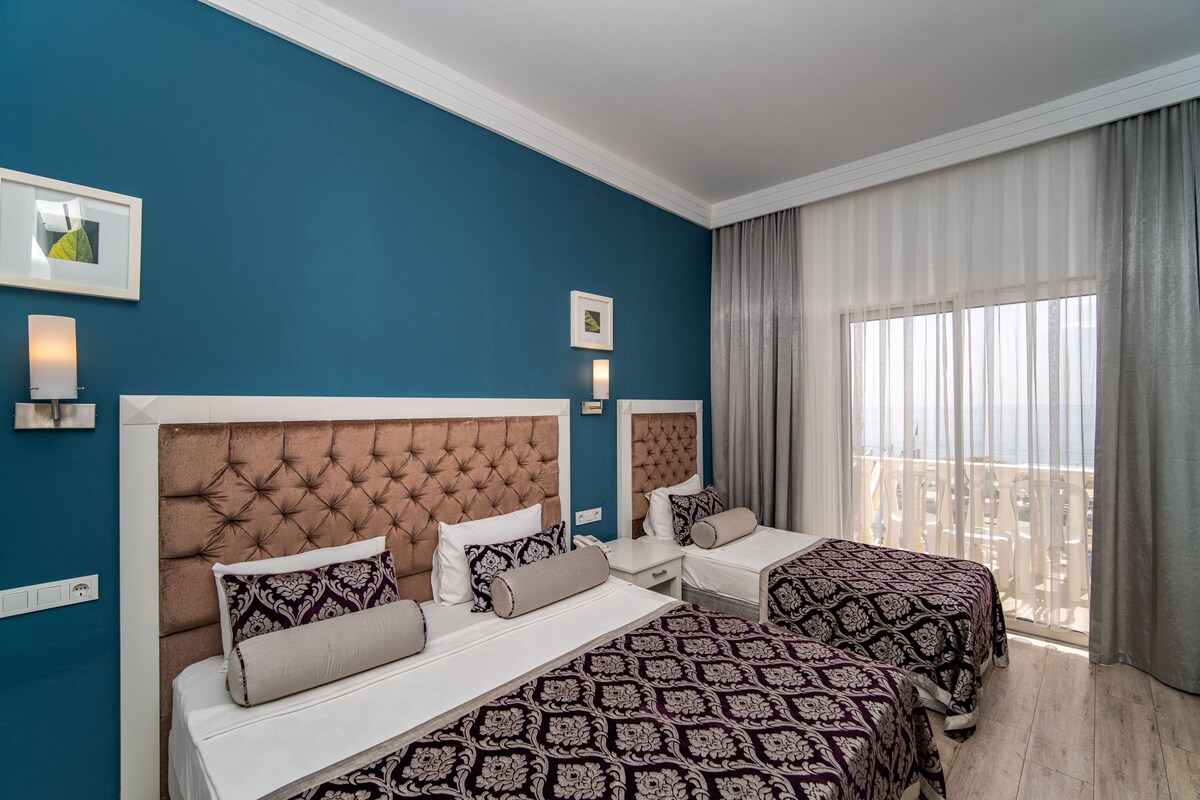 Habitación de hotel con dos camas, un ventanal con cortinas y obras de arte en las paredes.