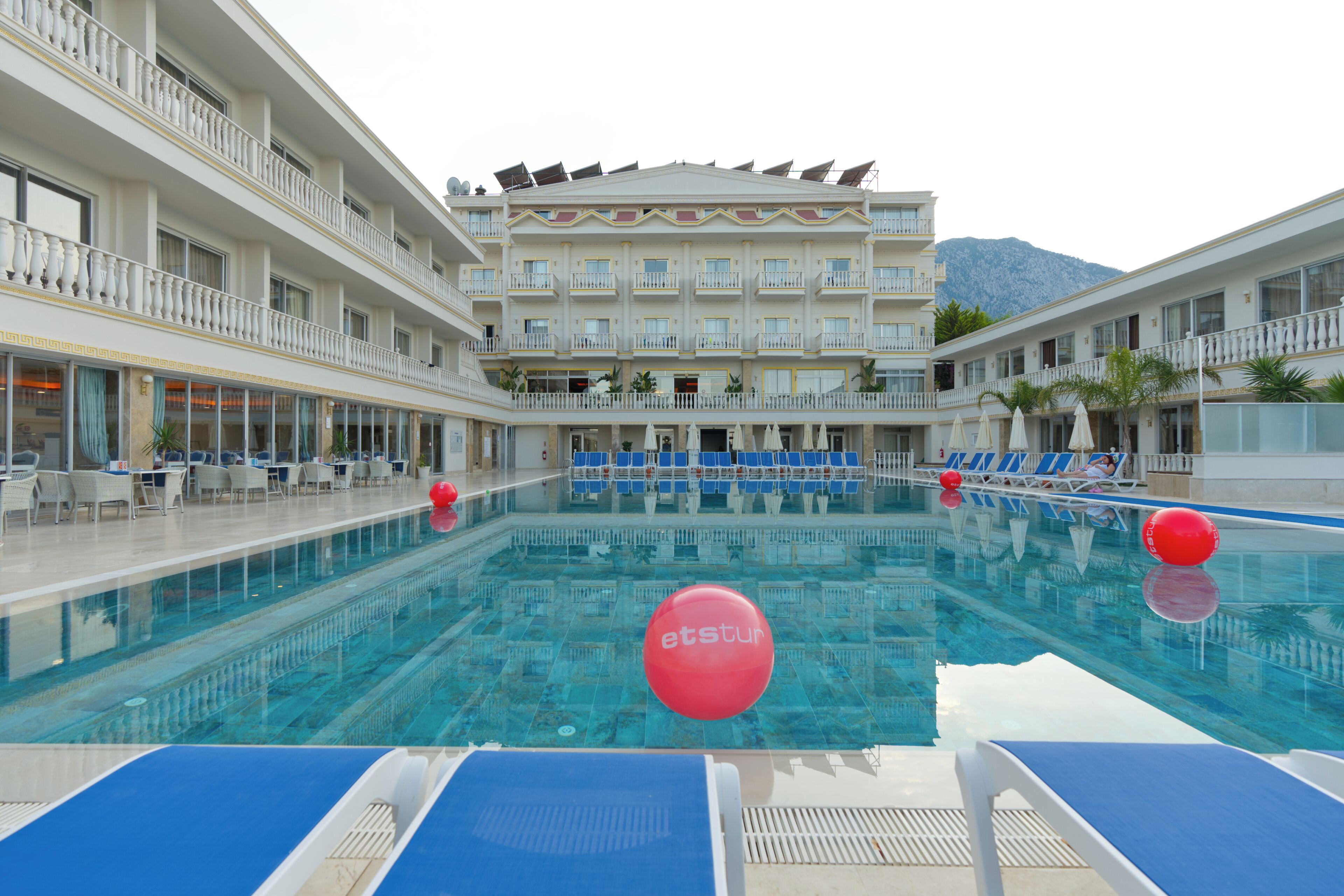 A hotel pool area with multiple levels, blue lounge chairs, and a clear view of the mountains in the background.