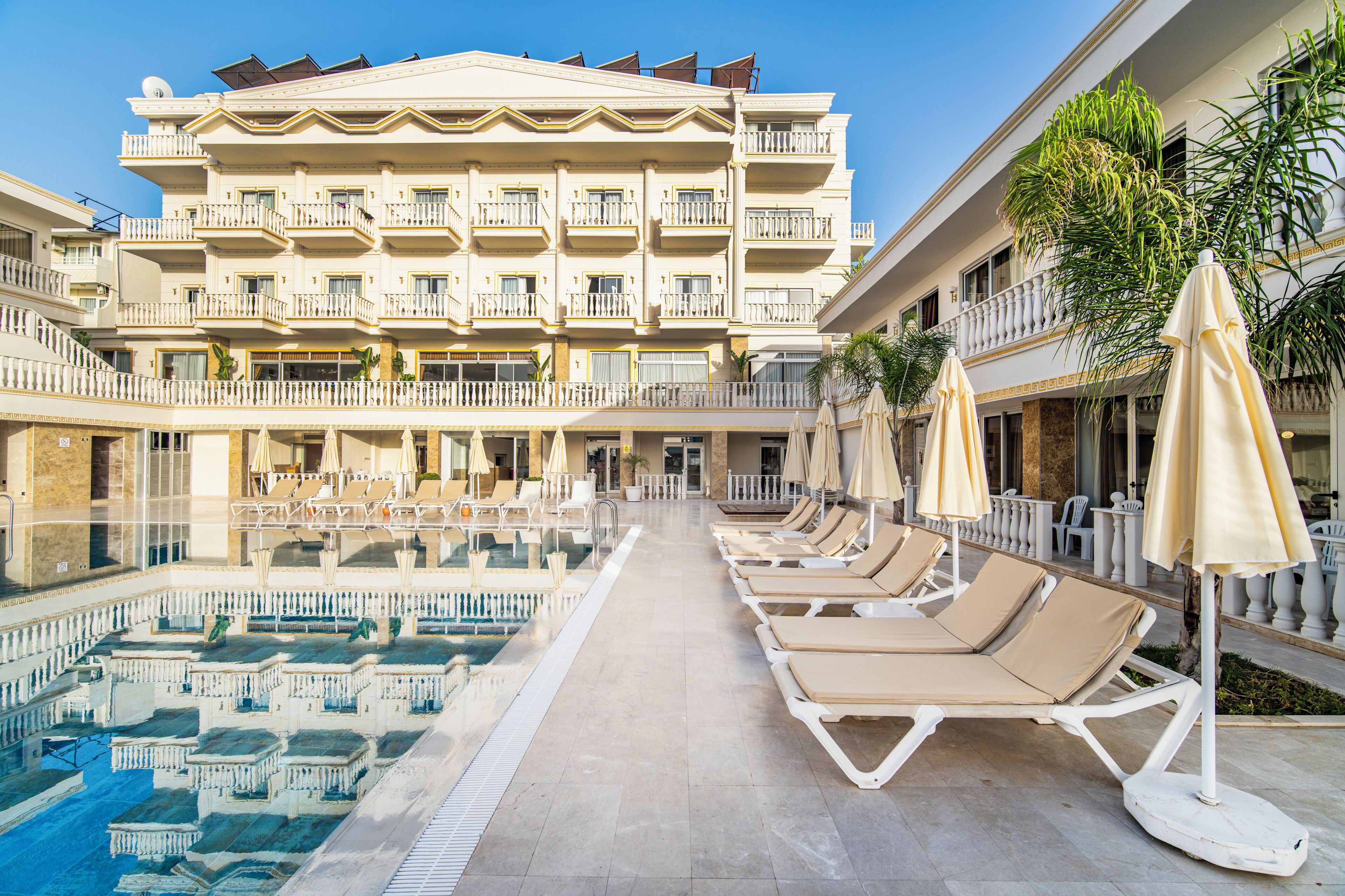 A hotel with a swimming pool, sun loungers, and a multi-story building with balconies.